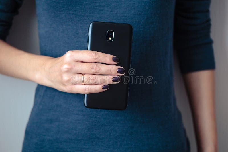 Black mobie smart phone in woman/s hands with perfect dark violet manicure over simple background. Black mobie smart phone in woman/s hands with perfect dark violet manicure over simple background