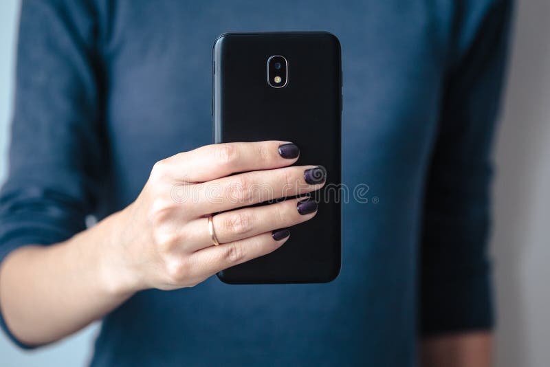 Black mobie smart phone in woman/s hands with perfect dark violet manicure over simple background. Black mobie smart phone in woman/s hands with perfect dark violet manicure over simple background