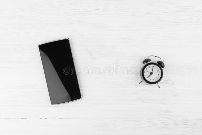 Teléfono elegante negro al lado del despertador con la alarma de Bell gemela en Wh fotografía de archivo Teléfono elegante negro al lado del despertador con la alarma de Bell gemela en Wh fotografía de archivo