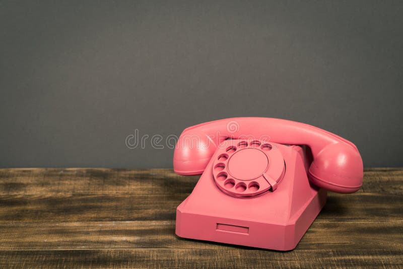 Teléfono rosado del vintage en la tabla de madera con el fondo de la pared del color imagen de archivo Teléfono rosado del vintage en la tabla de madera con el fondo de la pared del color imagen de archivo