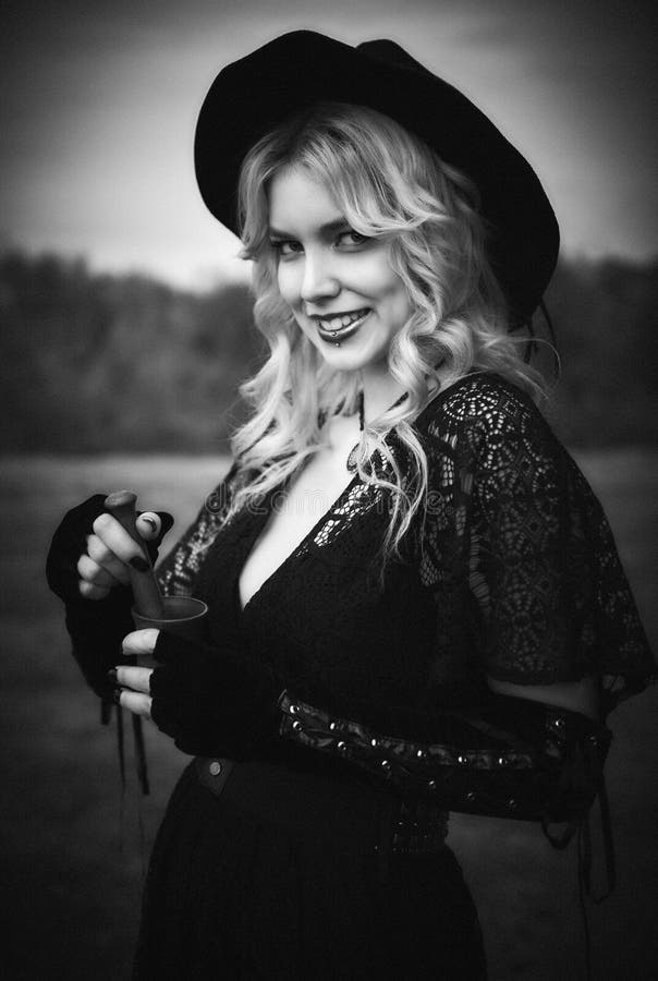 Tema de Halloween: bruja astuta moderna en vestido y sombrero negros con el mortero y la maja en manos Blanco y negro, el grano d imagen de archivo Tema de Halloween: bruja astuta moderna en vestido y sombrero negros con el mortero y la maja en manos Blanco y negro, el grano d imagen de archivo