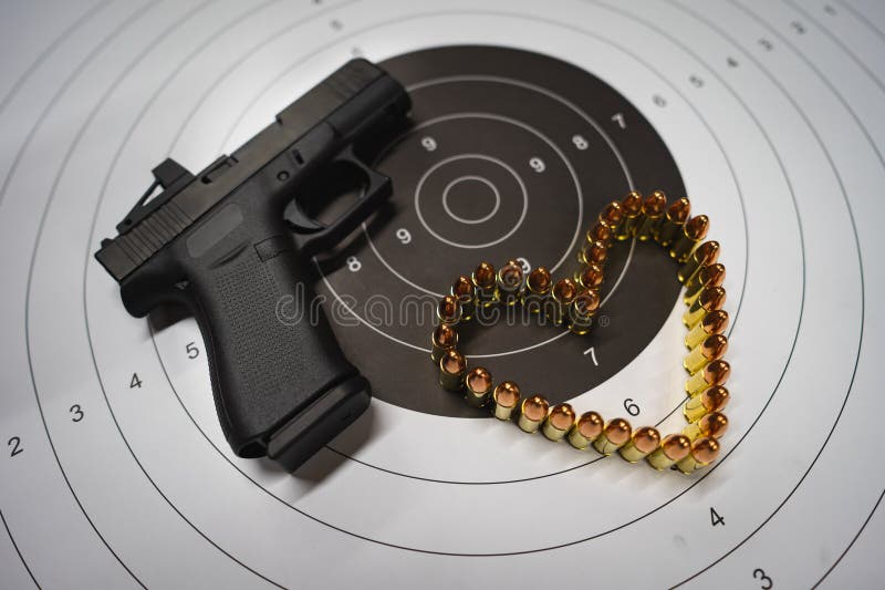 Tema del día de San Valentín y armas. una moderna pistola compacta con un punto rojo a blanco y un corazón hecho con cartuchos de foto de archivo libre de regalías