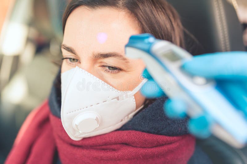 Temperature check point - the woman behind the wheel of the car in an anti-virus mask is subjected to temperature measurement