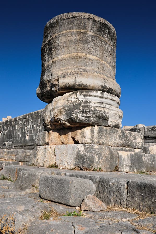 Columns in ruins of a Greek style temple. Bright sunlight, trees and blue sky and other surrounding buildings and elements. Columns in ruins of a Greek style temple. Bright sunlight, trees and blue sky and other surrounding buildings and elements.