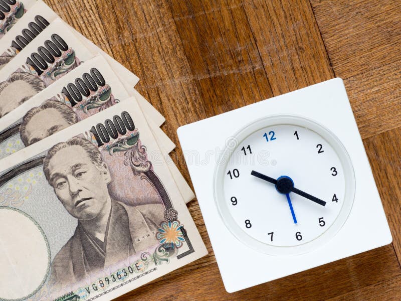 A clock and Japanese 10000 yen bills on the wooden table that depicts Time is money. A clock and Japanese 10000 yen bills on the wooden table that depicts Time is money