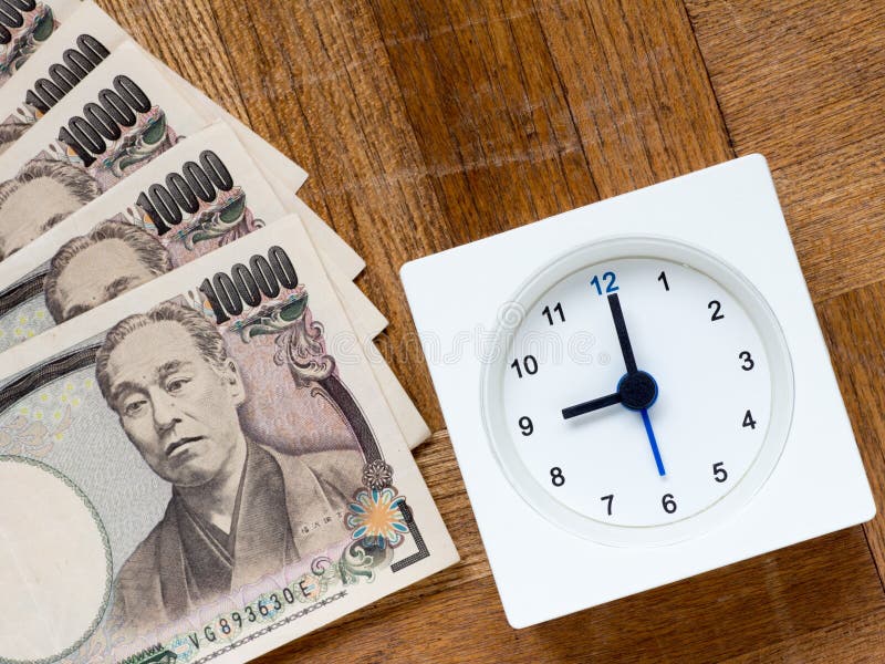 A clock and Japanese 10000 yen bills on the wooden table that depicts Time is money. A clock and Japanese 10000 yen bills on the wooden table that depicts Time is money