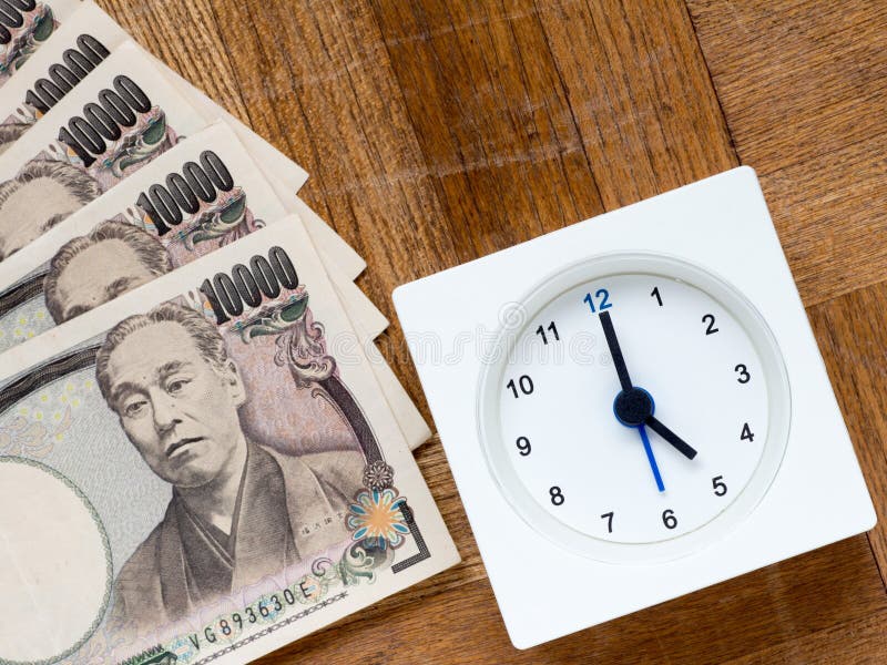 A clock and Japanese 10000 yen bills on the wooden table that depicts Time is money. A clock and Japanese 10000 yen bills on the wooden table that depicts Time is money