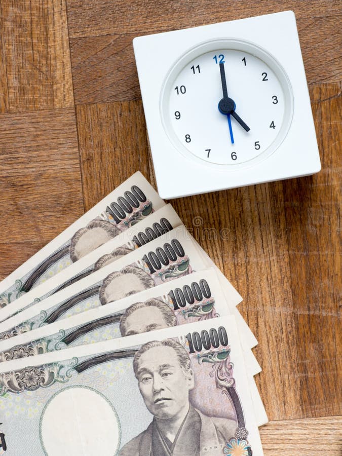 A clock and Japanese 10000 yen bills on the wooden table that depicts Time is money. A clock and Japanese 10000 yen bills on the wooden table that depicts Time is money