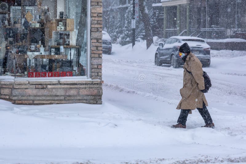 Montreal, CA - 2 February 2021: Man with protective face mask walking on the street during heavy snowfall. Montreal, CA - 2 February 2021: Man with protective face mask walking on the street during heavy snowfall