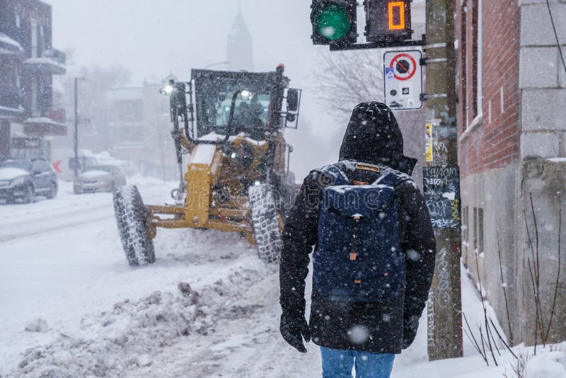 Montreal, CA - 2 February 2021: Man walking on the street during heavy snowfall with snowplough in background. Montreal, CA - 2 February 2021: Man walking on the street during heavy snowfall with snowplough in background