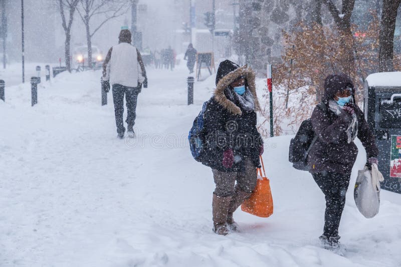 Montreal, CA - 2 February 2021: People with protective face masks walking on the street during heavy snowfall. Montreal, CA - 2 February 2021: People with protective face masks walking on the street during heavy snowfall