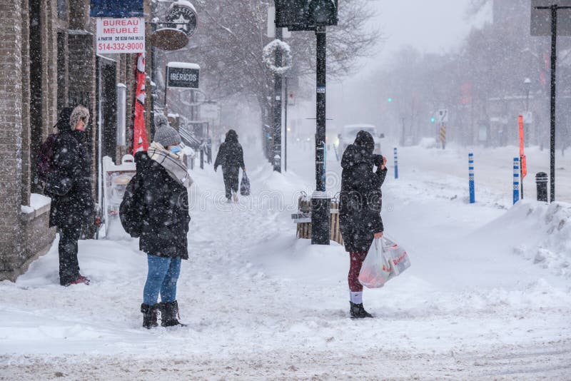 Montreal, CA - 2 February 2021: People with protective face masks walking on the street during heavy snowfall. Montreal, CA - 2 February 2021: People with protective face masks walking on the street during heavy snowfall