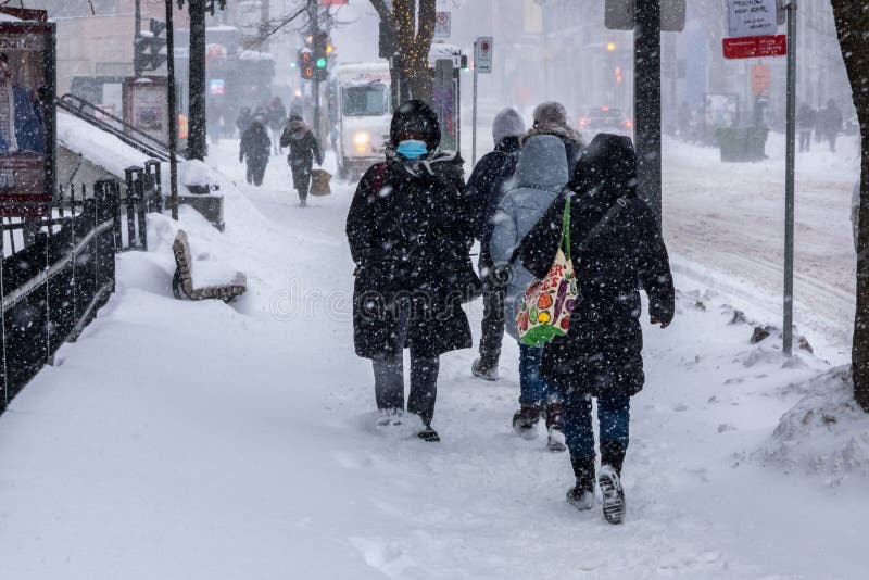 Montreal, CA - 2 February 2021: People with protective face masks walking on the street during heavy snowfall. Montreal, CA - 2 February 2021: People with protective face masks walking on the street during heavy snowfall