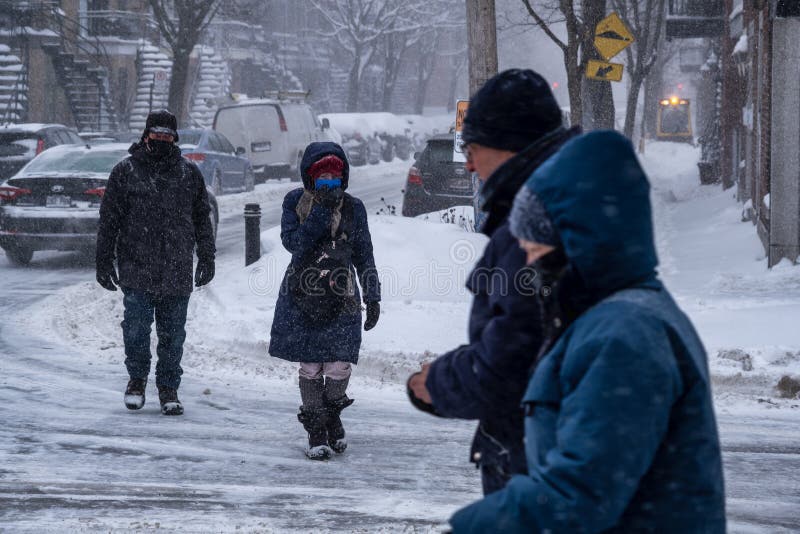 Montreal, CA - 2 February 2021: People with protective face masks walking on the street during heavy snowfall. Montreal, CA - 2 February 2021: People with protective face masks walking on the street during heavy snowfall