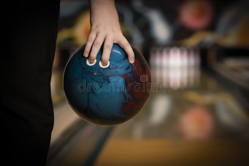 Ten pin bowling ball being held in hand close up, with bowling lane and pins background