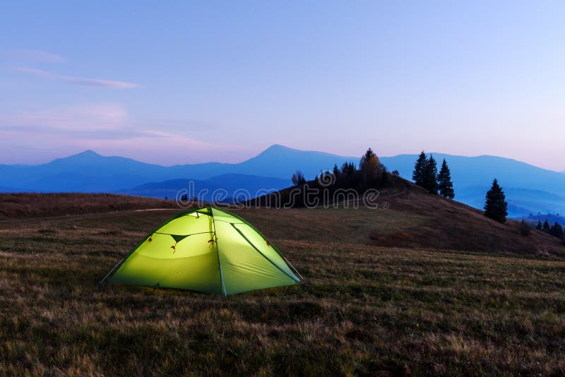 Tenda verde accesa dall'interno. La tenda verde si è accesa dall'interno da una torcia elettrica contro il contesto di un paesaggio incredibile della montagna Altopiano stupefacente di sera Concetto di turismo