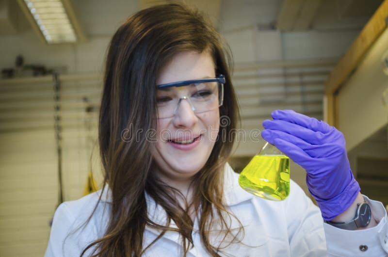 Tenencia feliz del cient?fico de la mujer y pagar cierre de la atenci?n hasta una soluci?n qu?mica amarilla en laboratorio de qu? fotos de archivo Tenencia feliz del cient?fico de la mujer y pagar cierre de la atenci?n hasta una soluci?n qu?mica amarilla en laboratorio de qu? fotos de archivo