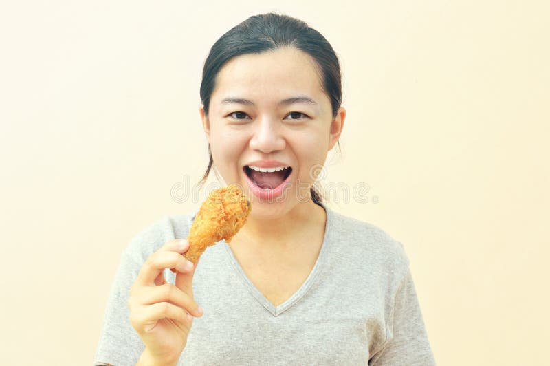 Tenencia feliz joven de la mujer y consumición del pollo de las fritadas foto de archivo