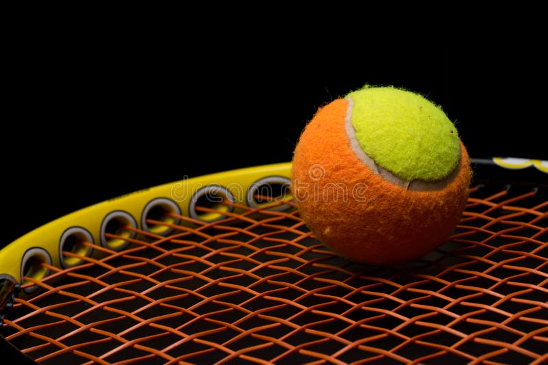 Tennis ball for kids with tennis racket with green grip handle and orange strings on black background