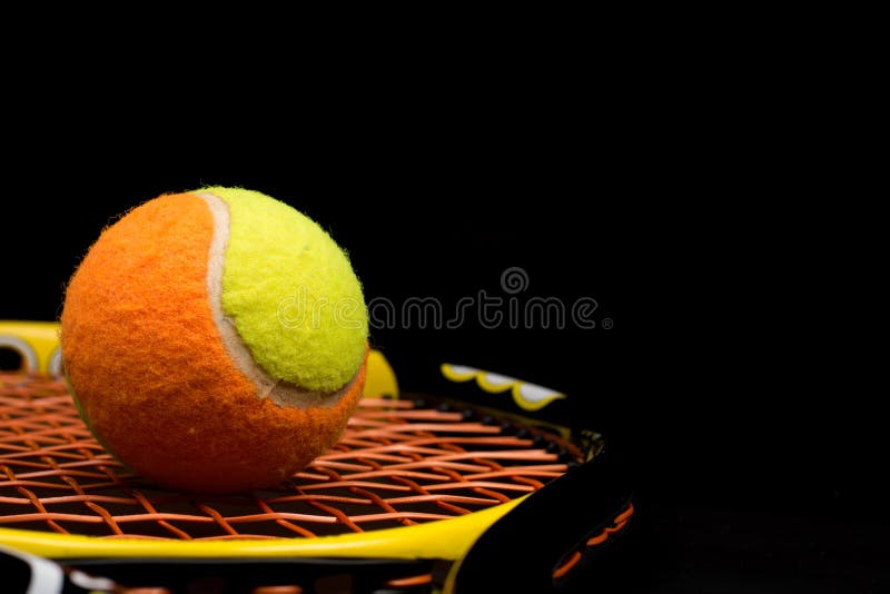 Tennis ball for kids with tennis racket with green grip handle and orange strings on black background