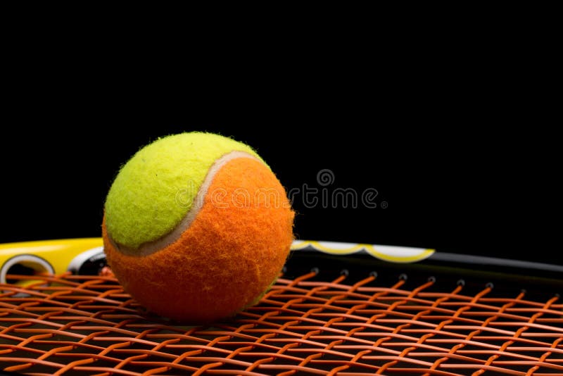 Tennis ball for kids with tennis racket with green grip handle and orange strings on black background