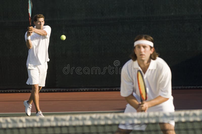 Tennis Player Hitting Backhand; doubles partner squatting at net