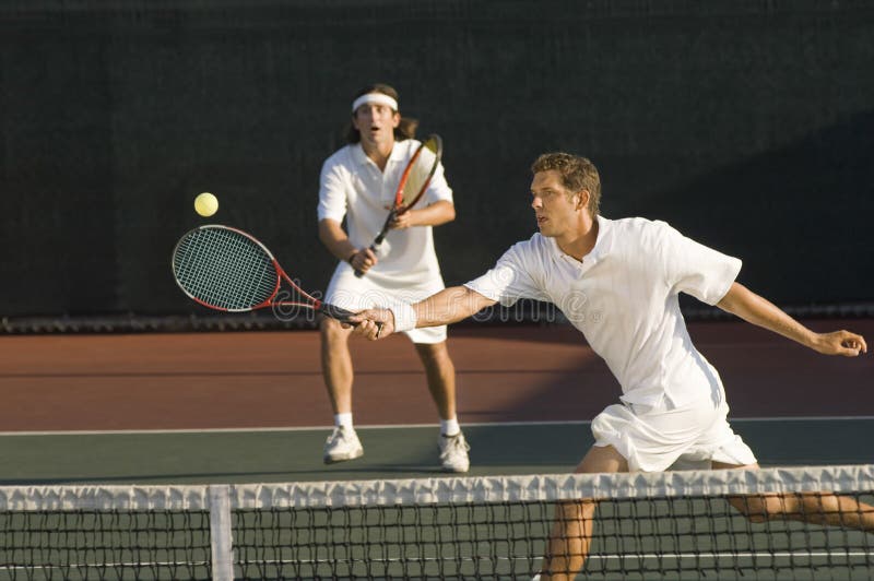 Young male tennis player hitting ball with doubles partner standing in background