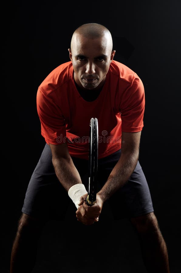 A portrait of a tanned sportive tennis player with a racket against black background. tennis player portrait.