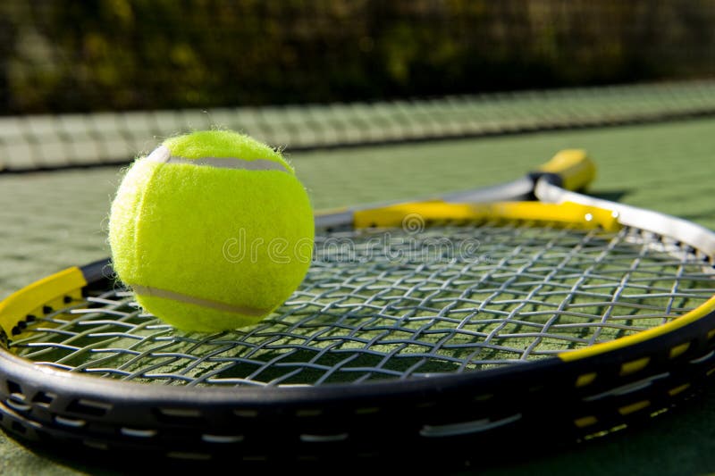 A tennis racket and new tennis ball on a freshly painted tennis court. A tennis racket and new tennis ball on a freshly painted tennis court