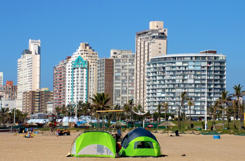 DURBAN, SOUTH AFRICA - MAY 3, 2014: Many people and green tents pitched on North beach against city skyline in Durban South Africa. DURBAN, SOUTH AFRICA - MAY 3, 2014: Many people and green tents pitched on North beach against city skyline in Durban South Africa