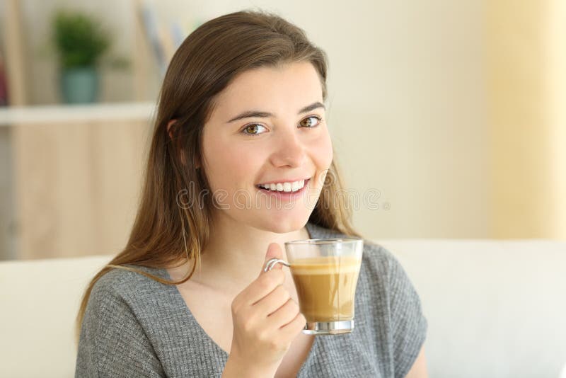 Tenuta teenager felice un caffè con latte che vi esamina fotografia stock Tenuta teenager felice un caffè con latte che vi esamina fotografia stock