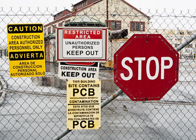 Warning signs outside hazardous industrial site announcing that it is a restricted construction area containing dangerous chemicals PCBs. Warning signs outside hazardous industrial site announcing that it is a restricted construction area containing dangerous chemicals PCBs.