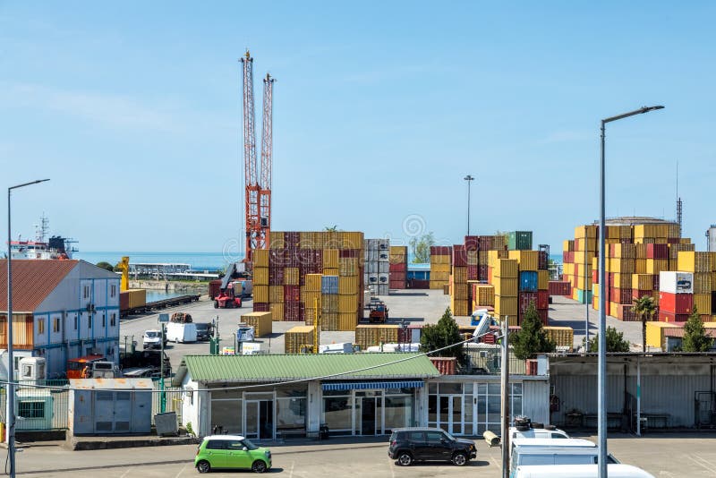 Terminal de port maritim cu macarale roșii, cu containere colorate stivuiesc clădiri de porturi și nave vizibile în fundal lângă m stock photo