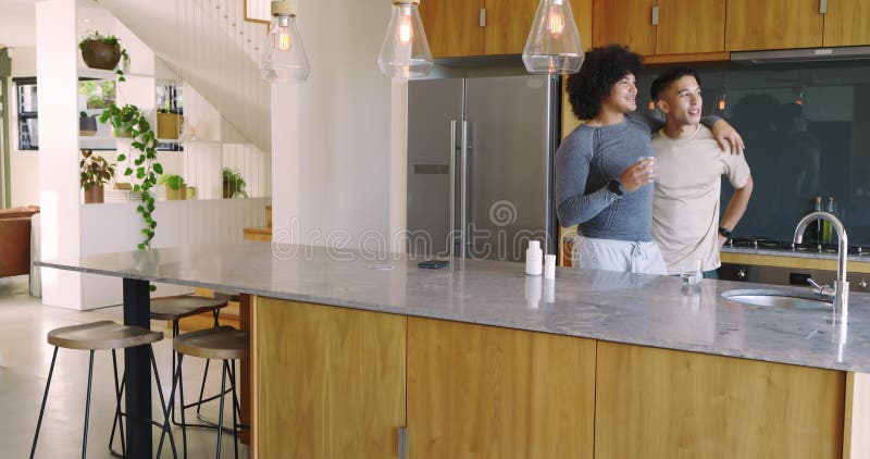 Terminando bebidas y compartiendo gestos cercanos, varios hombres de pareja se inclinan en la isla de la cocina riendo almacen de metraje de vídeo