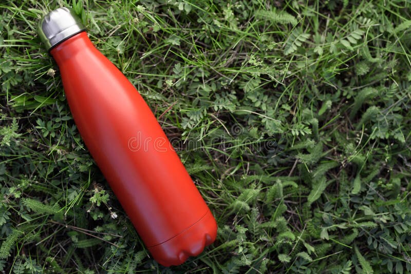 Termo inoxidable de la botella, color rojo En el fondo de la hierba verde foto de archivo libre de regalías Termo inoxidable de la botella, color rojo En el fondo de la hierba verde foto de archivo libre de regalías