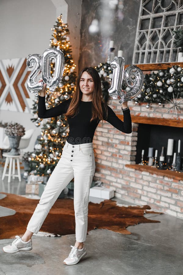 A terra arrendada feliz da mulher da menina do sorriso entrega os balões de ano novo na sala decorada com árvore e chaminé de Nat foto de stock A terra arrendada feliz da mulher da menina do sorriso entrega os balões de ano novo na sala decorada com árvore e chaminé de Nat foto de stock