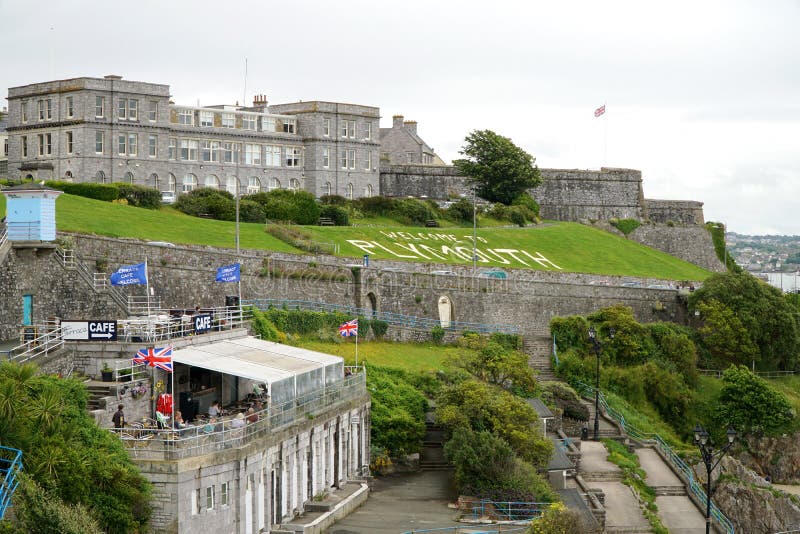 PLYMOUTH, UK - JULY 4 2016: Tourists sit in an outdoor cafe and walk along the public promenade in the British south coast seaport city of Plymouth, Devon. The Royal Citadel and a grass sign reading Welcome to Plymouth are in the background. PLYMOUTH, UK - JULY 4 2016: Tourists sit in an outdoor cafe and walk along the public promenade in the British south coast seaport city of Plymouth, Devon. The Royal Citadel and a grass sign reading Welcome to Plymouth are in the background.