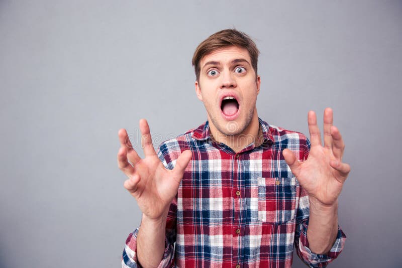 Portrait of terrified frightened young man in checkered shirt screaming with open mouth over grey background. Portrait of terrified frightened young man in checkered shirt screaming with open mouth over grey background