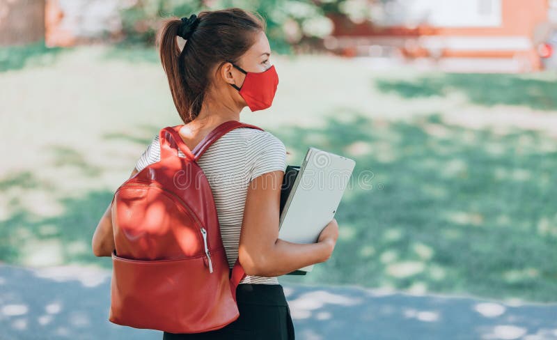 Terug naar school studente meisje met een covid masker op campus met rugzakboekjes en laptop. corona