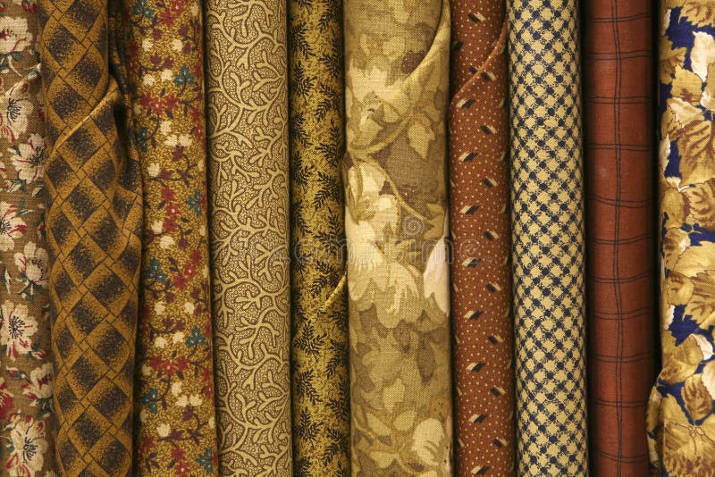 fabric bolts of quilt fabric in various designs in brown, gold, beige, and rust colored fabrics. fabric bolts of quilt fabric in various designs in brown, gold, beige, and rust colored fabrics