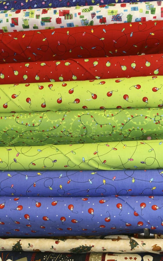 Bolts of bright christmas quilt fabric with tree lights, red ornaments, blue, packages, festive, holiday. Bolts of bright christmas quilt fabric with tree lights, red ornaments, blue, packages, festive, holiday