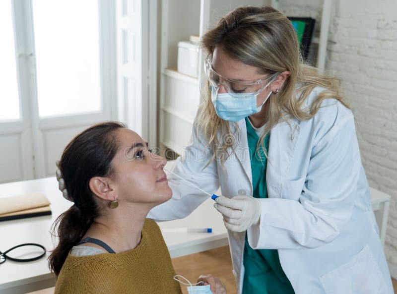 Nurse testing young adult women for coronavirus infection taking rapid COVID-19 test. Doctor performing nasal swab on female taking sample to analyze if patient is positive for infectious disease. Nurse testing young adult women for coronavirus infection taking rapid COVID-19 test. Doctor performing nasal swab on female taking sample to analyze if patient is positive for infectious disease