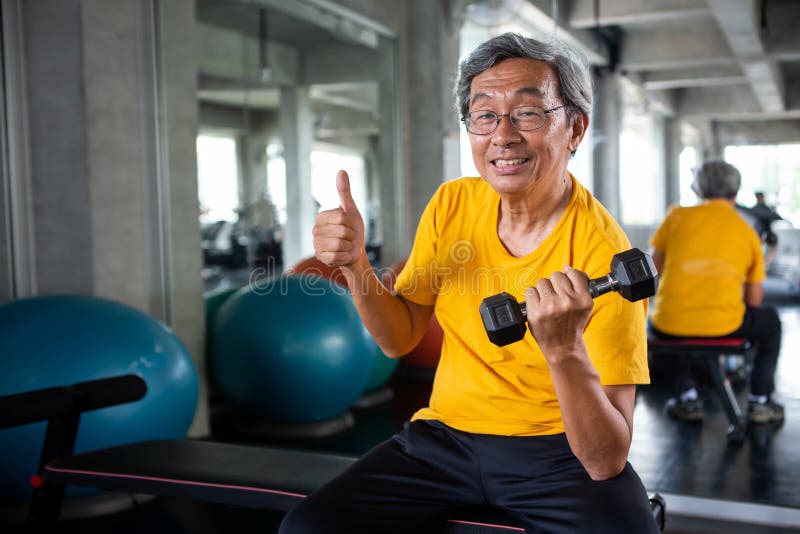 Teste di legno dell'uomo asiatico senior di sport e pollici di sollevamento di manifestazione su nella palestra di forma fisica m immagini stock Teste di legno dell'uomo asiatico senior di sport e pollici di sollevamento di manifestazione su nella palestra di forma fisica m immagini stock