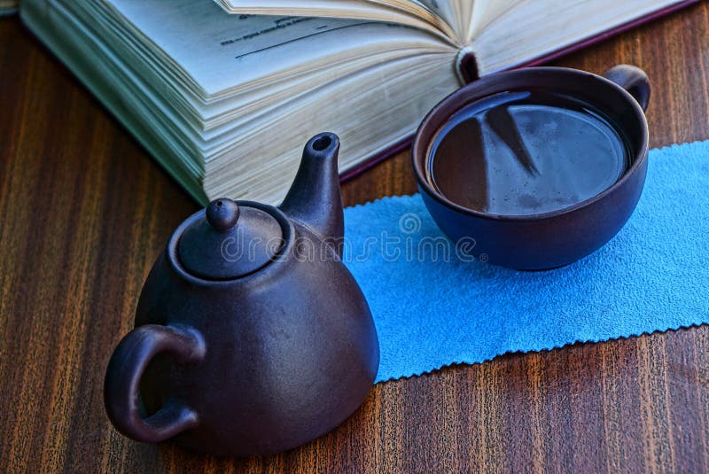 Tetera de Brown y una taza de agua cerca del libro abierto fotos de archivo libres de regalías Tetera de Brown y una taza de agua cerca del libro abierto fotos de archivo libres de regalías