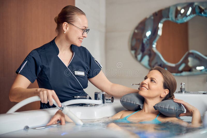 Young female therapist smiling at her patient during the hydrotherapy procedure in a spa salon. Young female therapist smiling at her patient during the hydrotherapy procedure in a spa salon