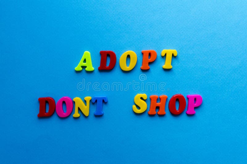 Text adopt don`t shop from plastic colored letters on blue paper background royalty free stock images