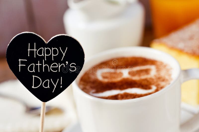 Closeup of a black heart-shaped signboard with the text happy fathers day written in it and a cup of cappuccino with a pair of eyeglasses and a moustache drawn with cocoa powder on its foam. Closeup of a black heart-shaped signboard with the text happy fathers day written in it and a cup of cappuccino with a pair of eyeglasses and a moustache drawn with cocoa powder on its foam