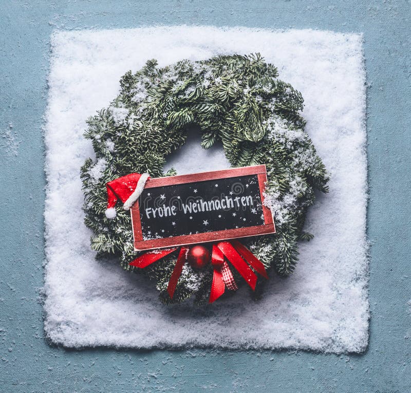 Texto de Frohe Weihnachten no alemão Grinalda do Natal com ramos verdes do abeto e sinal quadro vermelho e chapéu de Santa na nev imagens de stock royalty free Texto de Frohe Weihnachten no alemão Grinalda do Natal com ramos verdes do abeto e sinal quadro vermelho e chapéu de Santa na nev imagens de stock royalty free