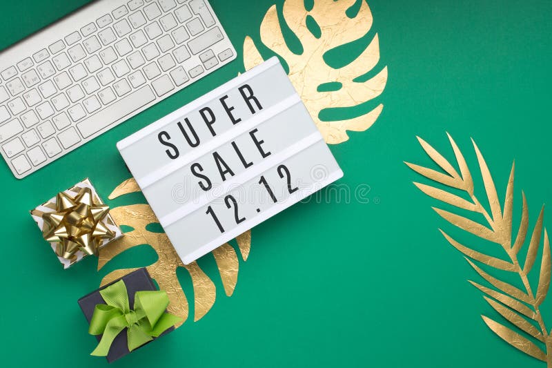 12.12 Super Sale text on white Lightbox, keyboard, computer mouse, gift box, gold tropical leaves Monstera, green paper background. Singles day concept. Online shopping of China. Top view, copy space. 12.12 Super Sale text on white Lightbox, keyboard, computer mouse, gift box, gold tropical leaves Monstera, green paper background. Singles day concept. Online shopping of China. Top view, copy space