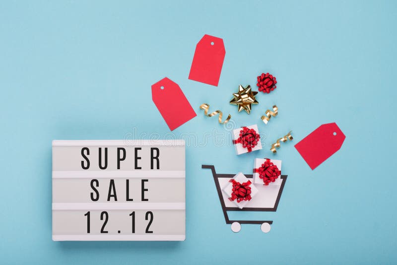 12.12 Super Sale text on white lightbox, shopping trolley, gift boxes and red tags on blue paper background. Double 12 Mega sales day concept. Top view, flat lay, copy space. 12.12 Super Sale text on white lightbox, shopping trolley, gift boxes and red tags on blue paper background. Double 12 Mega sales day concept. Top view, flat lay, copy space